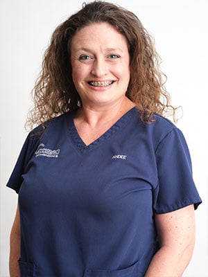 A brown haired woman in navy blue scrubs against a white background