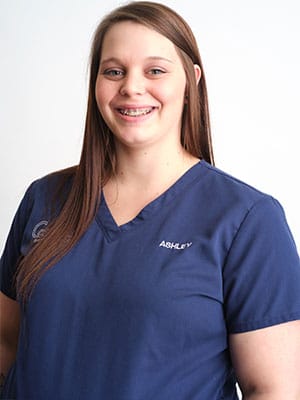 A brown haired woman in navy blue scrubs against a white background