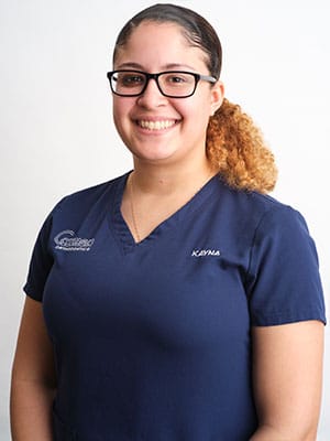 A woman with brown and blonde ombre hair in navy blue scrubs against a white background