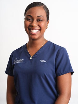 A black-haired woman in navy blue scrubs against a white background