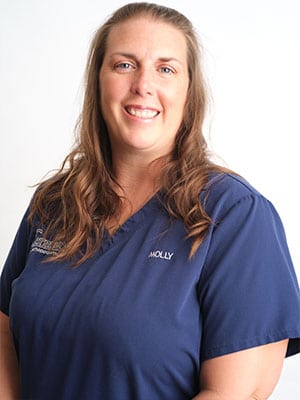 A brown-haired woman in navy blue scrubs against a white background