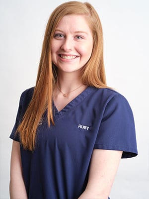 A red-haired woman in navy blue scrubs against a white background
