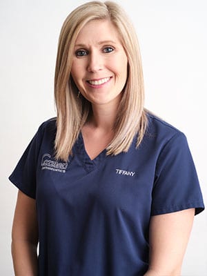 A blonde woman in navy blue scrubs against a white background