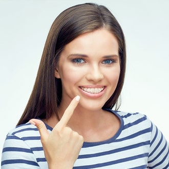 A girl with clear braces pointing to her mouth