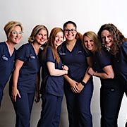 Six women in navy blue scrubs huddled together in a photo.