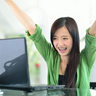 A girl in a green shirt and braces sitting at a computer with her arms up.