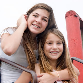 Two sisters with brown hair and braces on a playground.