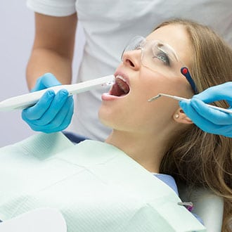 A patient opening her mouth for an orthodontist who is examining her with an iTero scanner.