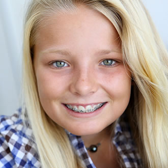Blonde girl with braces and blue checked shirt smiling at the camera.