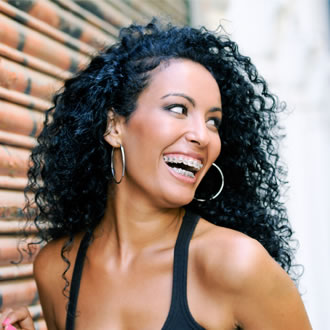 A girl with curly hair and braces smiling against a brick background
