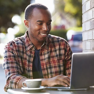 A man sitting at an outdoor cafe table with his laptop and a coffee.