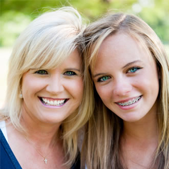 A blonde woman and a blonde girl with braces smiling outside.