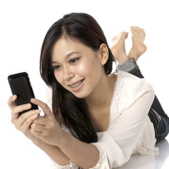 A woman with braces lying on her front, looking at her phone.
