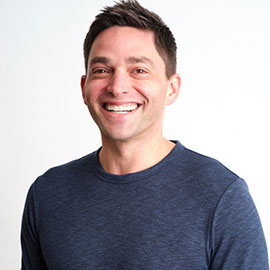 Smiling man with brown hair and a dark grey t-shirt against a white background.