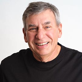 Smiling man with grey hair and a black t-shirt against a white background.