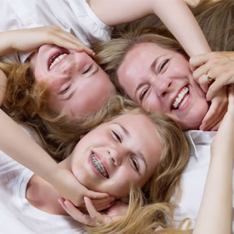A mom and two girls smiling laying on the floor with their heads together.