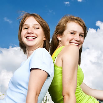 Two girls with auburn hair against a blue sky with clouds