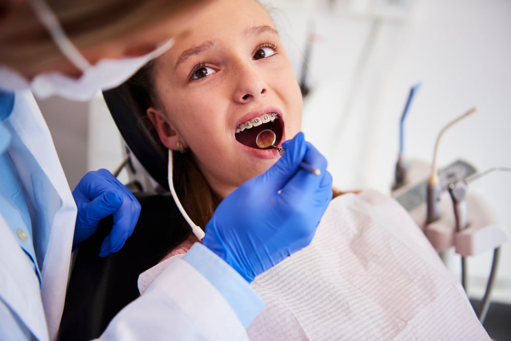 Teenage girl at an appointment looking expectantly up at the orthodontist as they examine her braces
