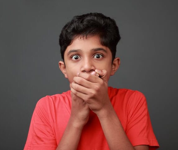 Child in bright red-orange tee shirt covering their mouth with both hands