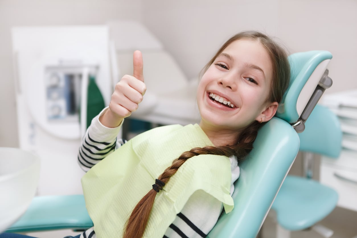 Smiling girl giving a thumbs up while being screened for early orthodontic treatment