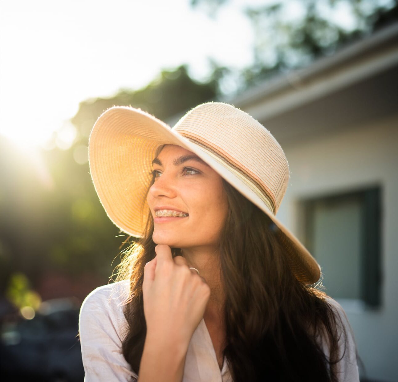 Adult with braces in Columbus, smiling up at the sky in a stylish hat