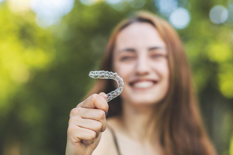 Teen with Invisalign Teen® in Columbus, Ohio, smiling while holding one of her aligners outside