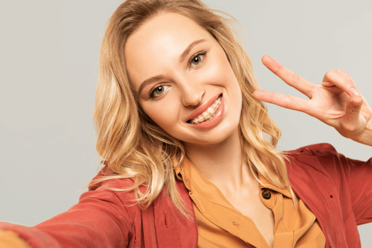 Teenager with ceramic clear braces in Columbus, Ohio making a peace sign in an orange shirt.