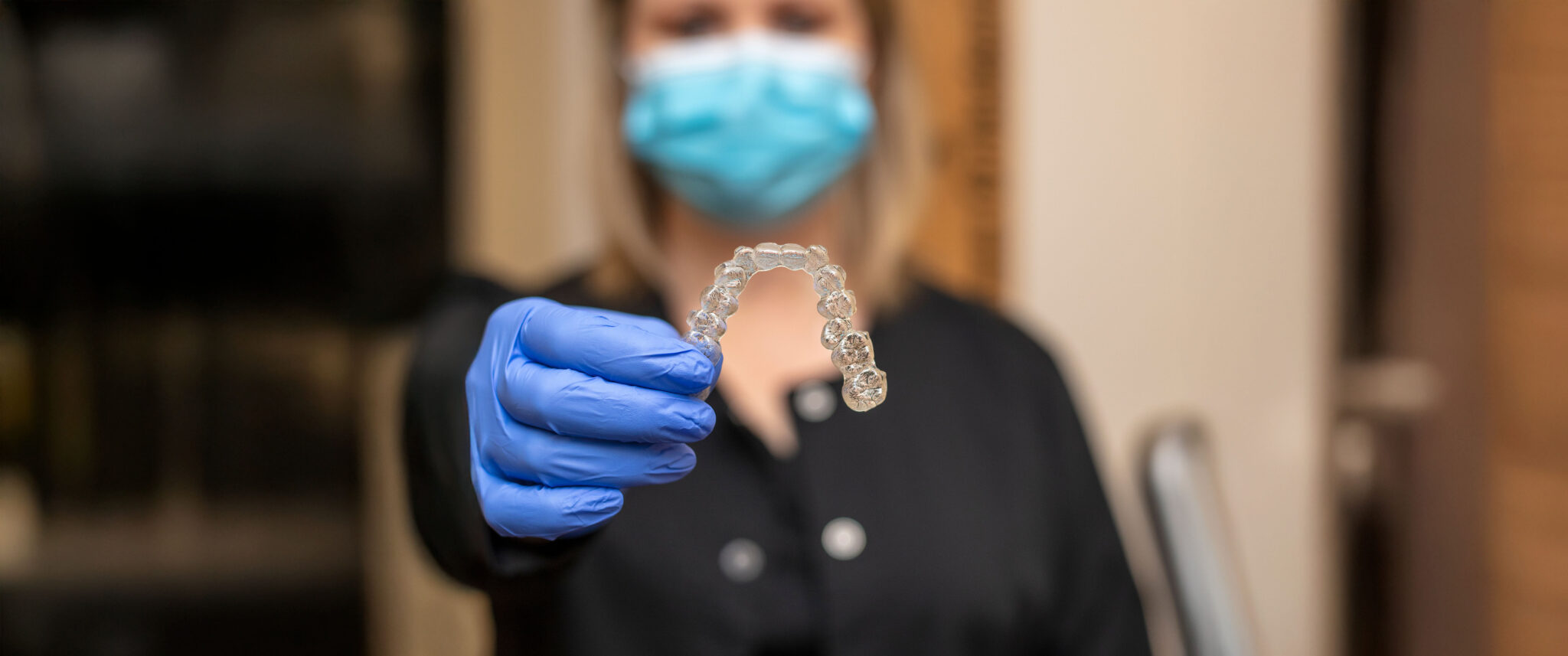 Orthodontic treatment professional holding an invisalign aligner while in a black top and PPE