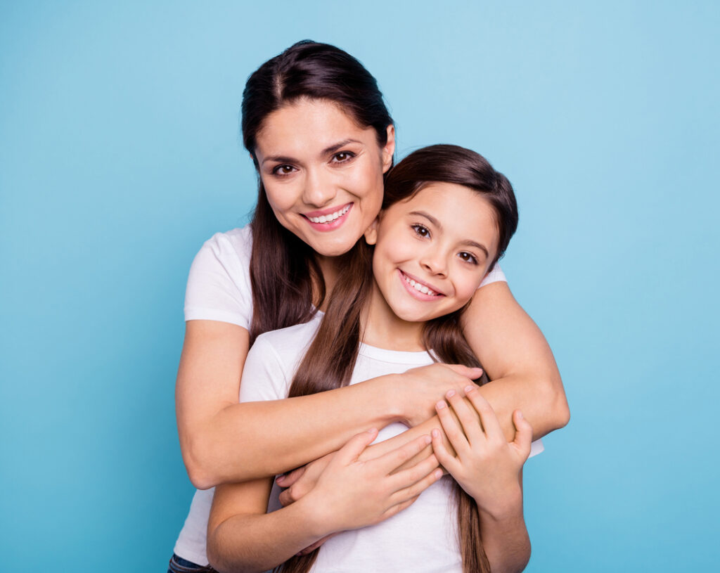 Mother smiling and embracing her daughter from behind