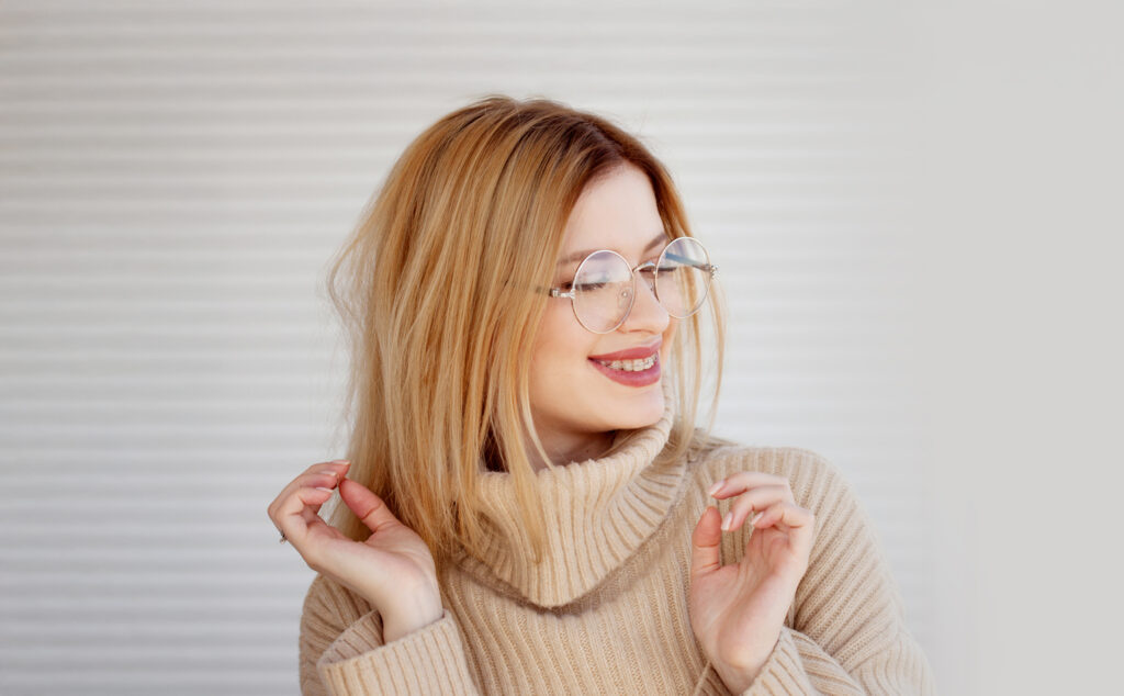 Stylish and beautiful young blonde in beige oversize sweater. Young woman with glasses, portrait
