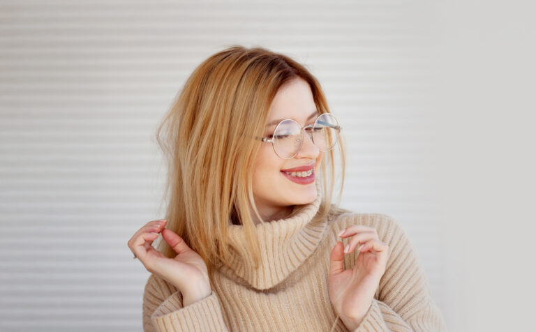 Stylish and beautiful young blonde in beige oversize sweater. Young woman with glasses, portrait