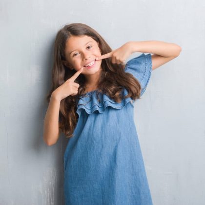 Young hispanic kid over grunge grey wall smiling confident showing and pointing with fingers teeth and mouth. Health concept.