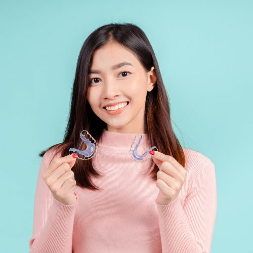 Young woman in a soft pink sweater holding a removable retainer in each hand