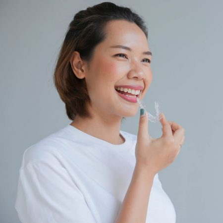 Young woman in a plain white tee shirt smiling and holding an invisible aligner