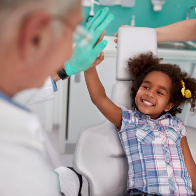 Small girl giving a high five while being screened for interceptive orthodontic treatment